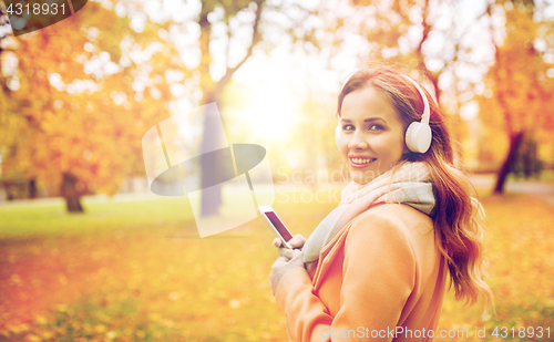 Image of woman with smartphone and earphones in autumn park