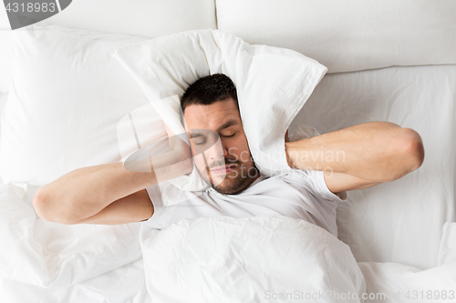 Image of man in bed with pillow suffering from noise