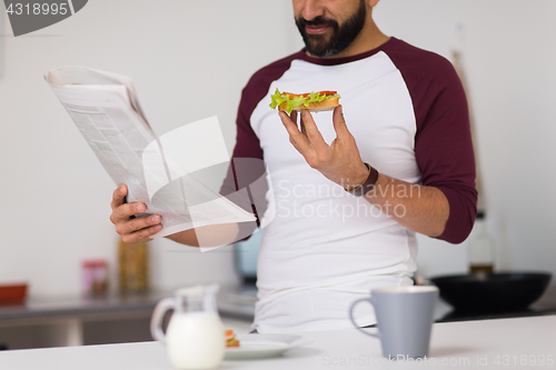 Image of man reading newspaper and eating at home kitchen