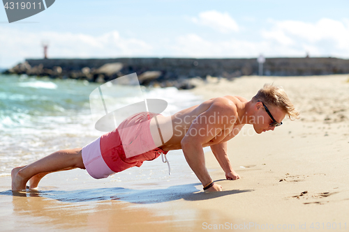 Image of young man doing push-ups on summer beach