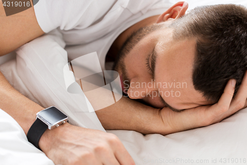 Image of close up of man with smartwatch sleeping in bed