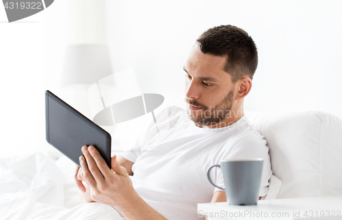 Image of young man with tablet pc in bed at home bedroom