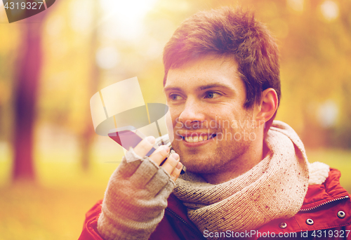 Image of man recording voice on smartphone at autumn park