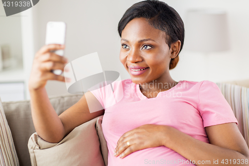 Image of pregnant woman taking smartphone selfie at home