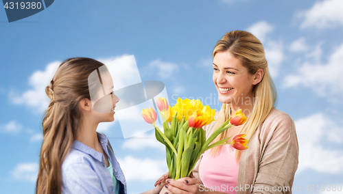 Image of happy girl giving flowers to mother over blue sky