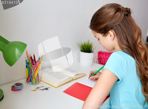 Image of happy girl with book writing to notebook at home