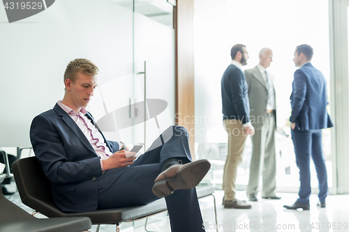 Image of Businessman using smart phone while sitting in waiting room.