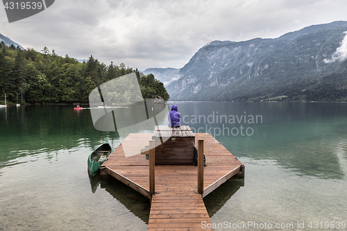 Image of Woman wearing purple hoodie watching tranquil overcast morning scene at lake Bohinj, Alps mountains, Slovenia.