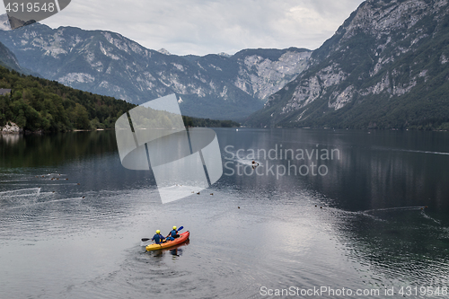 Image of People rowing in the canoe on tranquil overcast morning at lake Bohinj, Alps mountains, Slovenia.