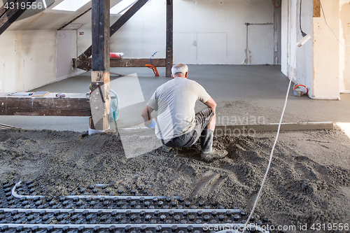 Image of Laborer leveling sand and cement screed over floor heating.