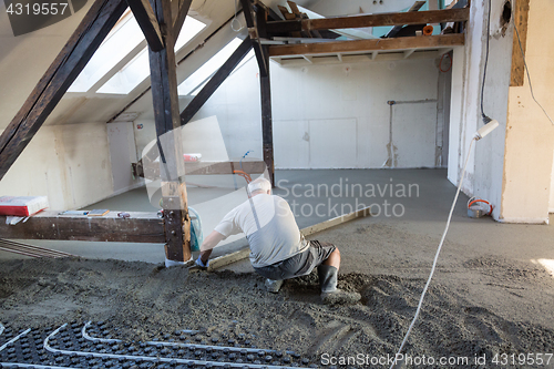 Image of Laborer leveling sand and cement screed over floor heating.