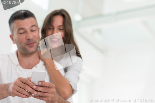 Image of happy couple using mobile phone at home