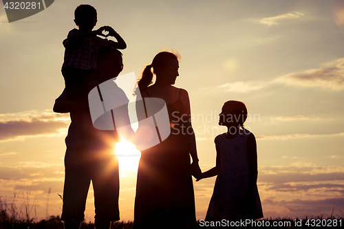 Image of Happy family standing on the field at the sunset time.