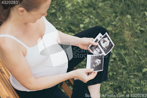 Image of pregnant woman sitting on the bench and loocking ultrasound scan