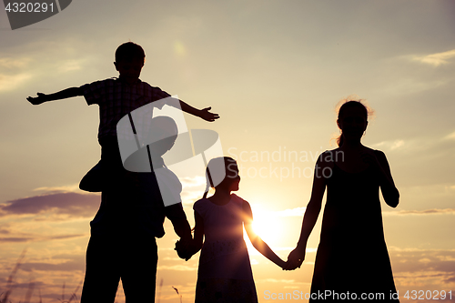 Image of Happy family standing on the field at the sunset time.