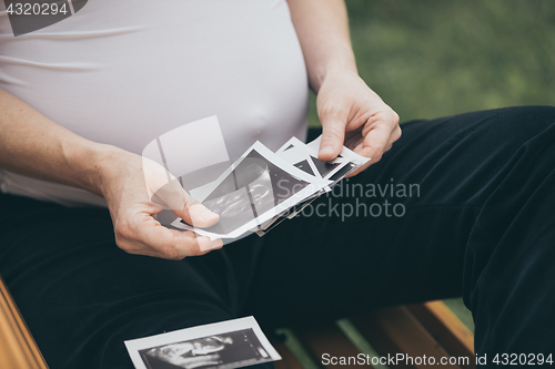 Image of pregnant woman sitting on the bench and loocking ultrasound scan