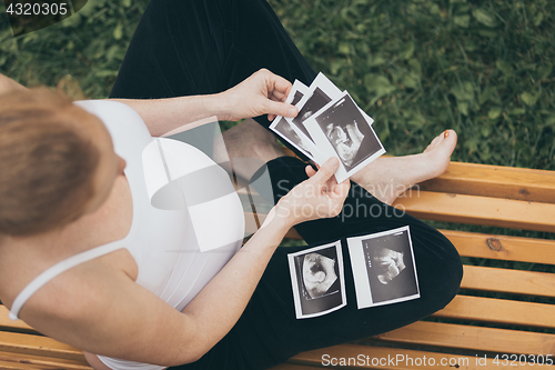 Image of pregnant woman sitting on the bench and loocking ultrasound scan