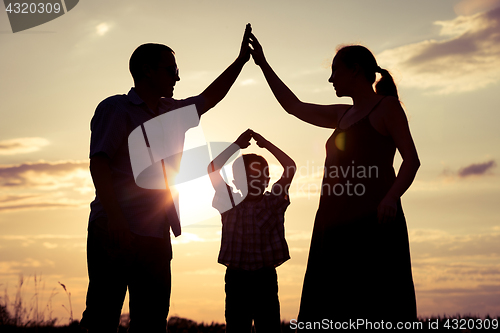 Image of Happy family standing on the field at the sunset time.