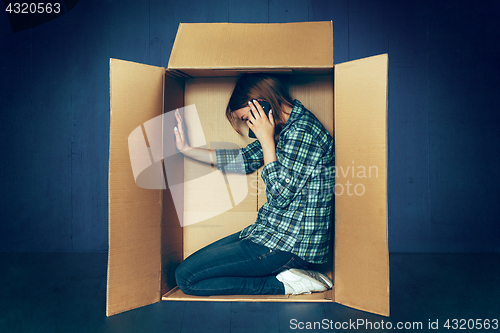Image of Introvert concept. Woman sitting inside box and working with phone