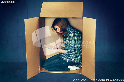 Image of Introvert concept. Woman sitting inside box and working with laptop