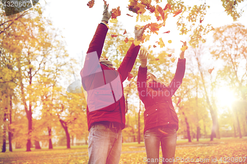 Image of happy young couple throwing autumn leaves in park