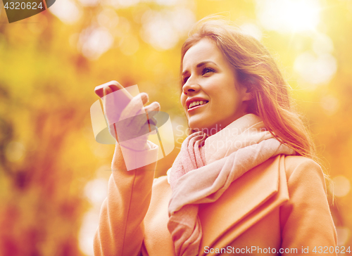 Image of woman recording voice on smartphone in autumn park