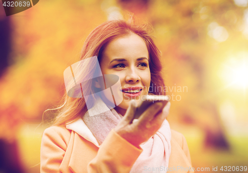 Image of woman recording voice on smartphone in autumn park