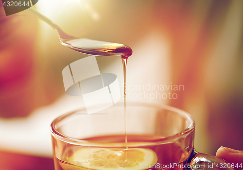 Image of close up of woman adding honey to tea with lemon