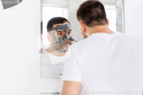 Image of young man applying clay mask to face at bathroom