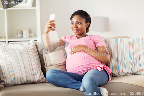 Image of pregnant woman taking smartphone selfie at home