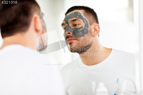 Image of young man with clay mask on face at bathroom