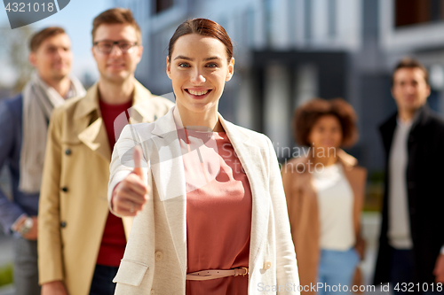 Image of happy smiling woman showing thumbs up outdoors