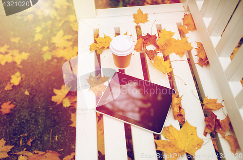 Image of tablet pc and coffee cup on bench in autumn park