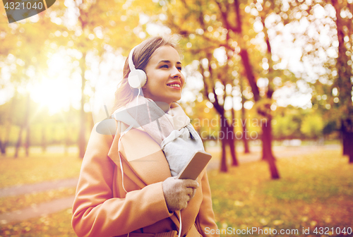 Image of woman with smartphone and earphones in autumn park