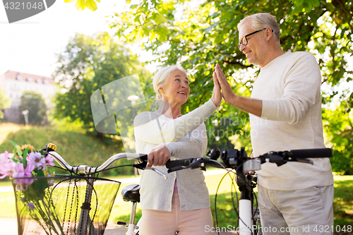Image of senior couple with bikes making high five at park