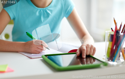 Image of girl with tablet pc writing to notebook at home