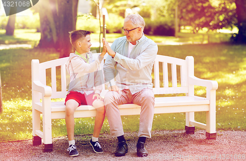 Image of old man and boy making high five at summer park