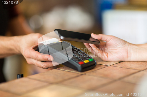 Image of hands with payment terminal and smartphone at bar