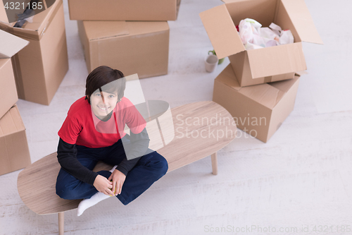 Image of boy sitting on the table with cardboard boxes around him top vie