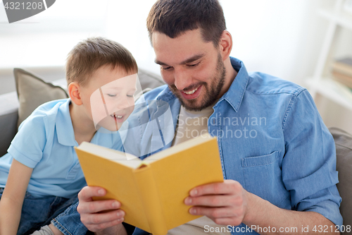 Image of happy father and son reading book sofa at home