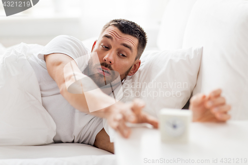 Image of young man in bed reaching for alarm clock