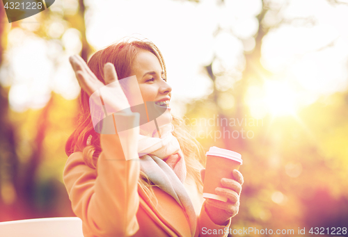 Image of happy young woman drinking coffee in autumn park