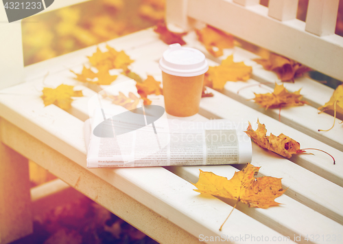 Image of newspaper and coffee cup on bench in autumn park