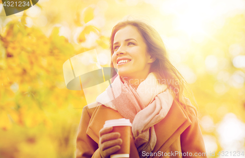 Image of happy young woman drinking coffee in autumn park