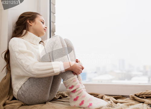 Image of sad girl sitting on sill at home window in winter