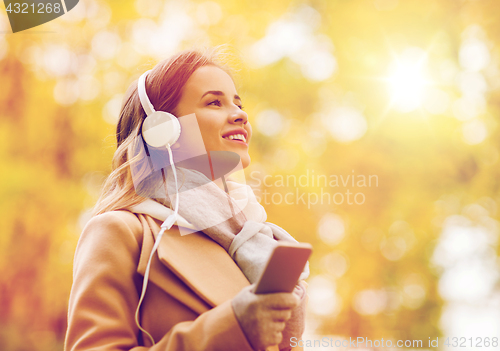 Image of woman with smartphone and earphones in autumn park