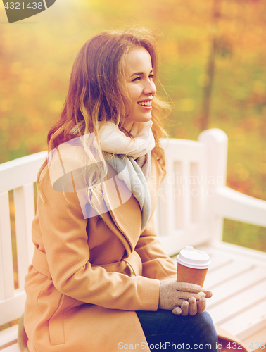 Image of happy young woman drinking coffee in autumn park