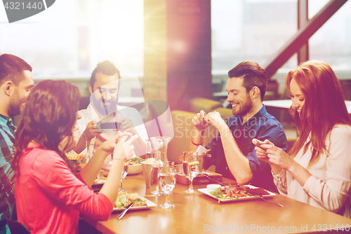 Image of happy friends taking picture of food at restaurant