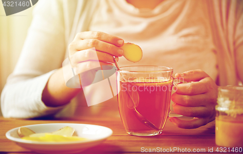 Image of close up of woman adding ginger to tea with lemon