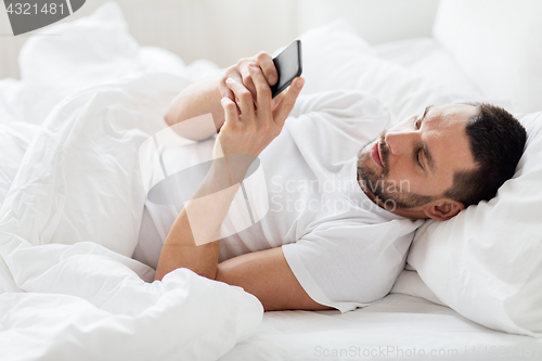 Image of young man with smartphone in bed in morning